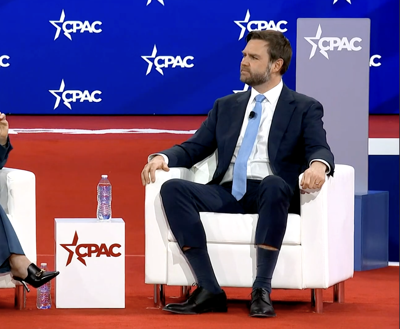JD Vance sits in a chair at CPAC, wearing what appears to be the businessman equivalent of skinny jeans. His cuffs have hiked up above his socks, and there is no rational explanation for the slenderness of the cut.